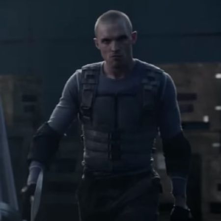 Ed Skrein is walking intensely while holding an axe on each of his hand.